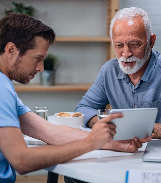 caregiver-showing-tablet-to-senior-patient-at-home Caregiver reviewing information on a tablet with an elderly man at home