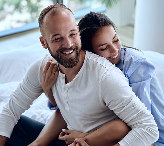 happy-couple-embracing-affectionately-in-bedroom Smiling couple embracing affectionately together in bed
